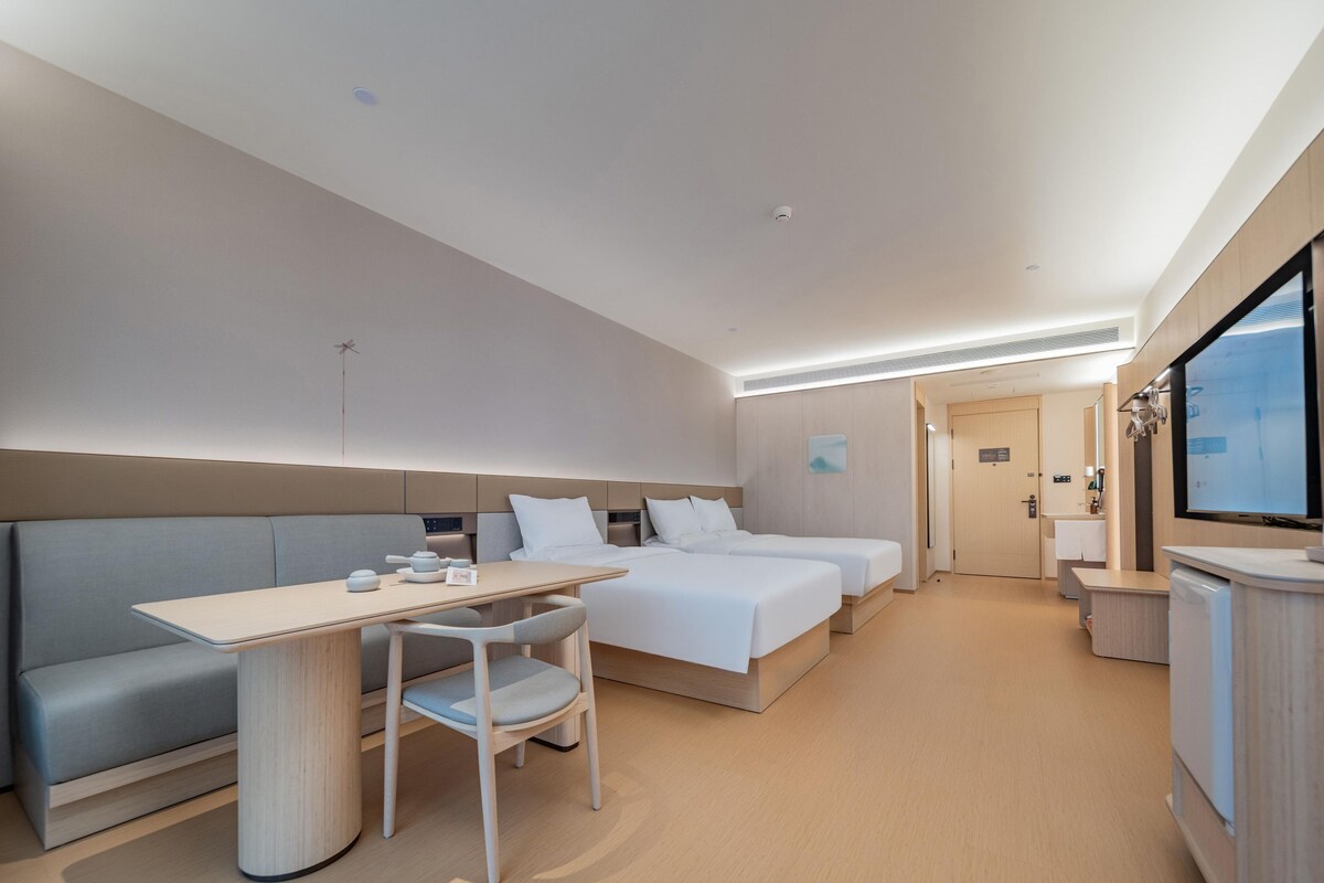 Quarto de hotel moderno com sofá, mesa de jantar, duas camas e televisão.