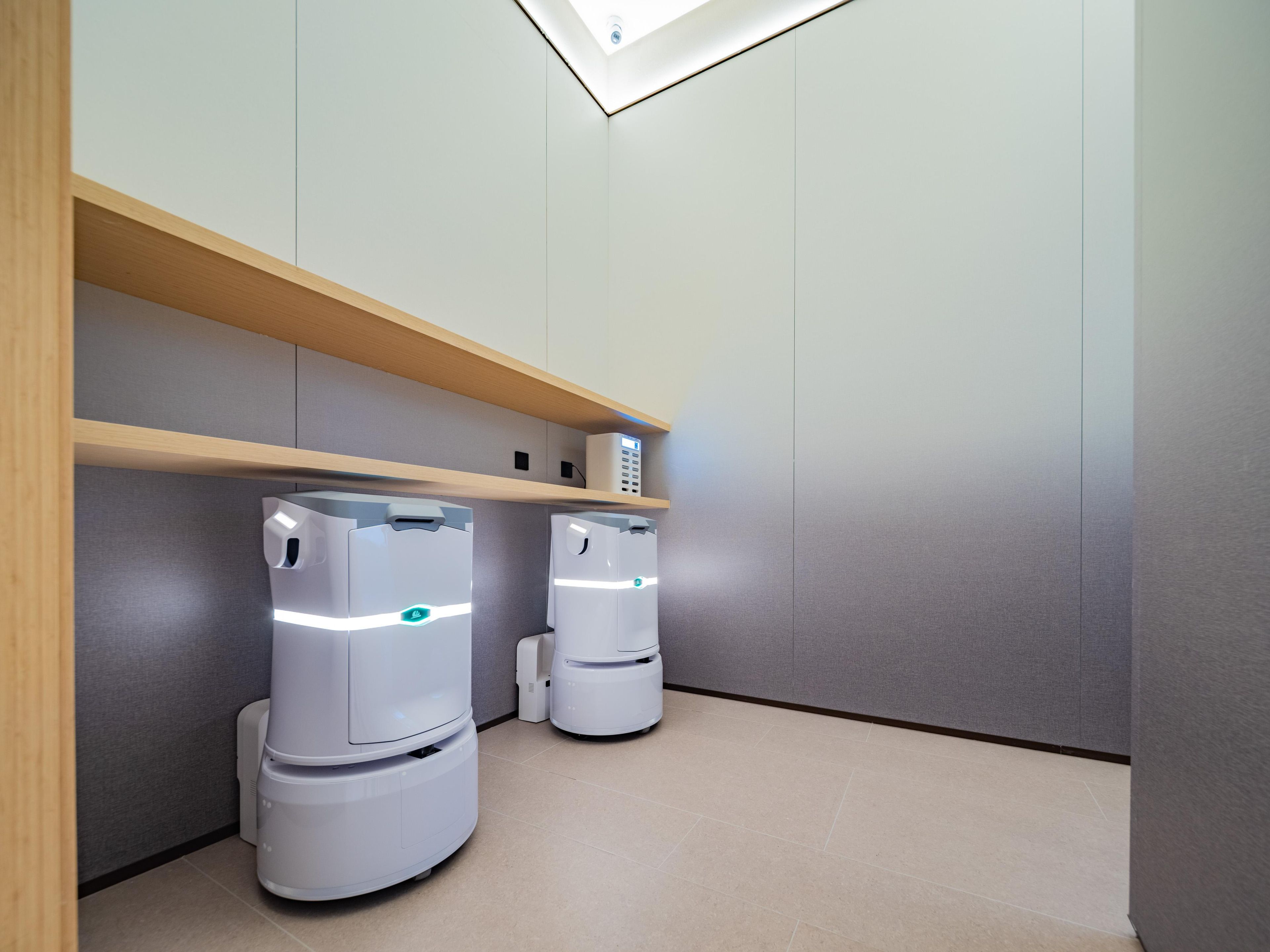 A modern bathroom with two white, cylindrical, self-cleaning toilets, a wooden shelf above, and a skylight.