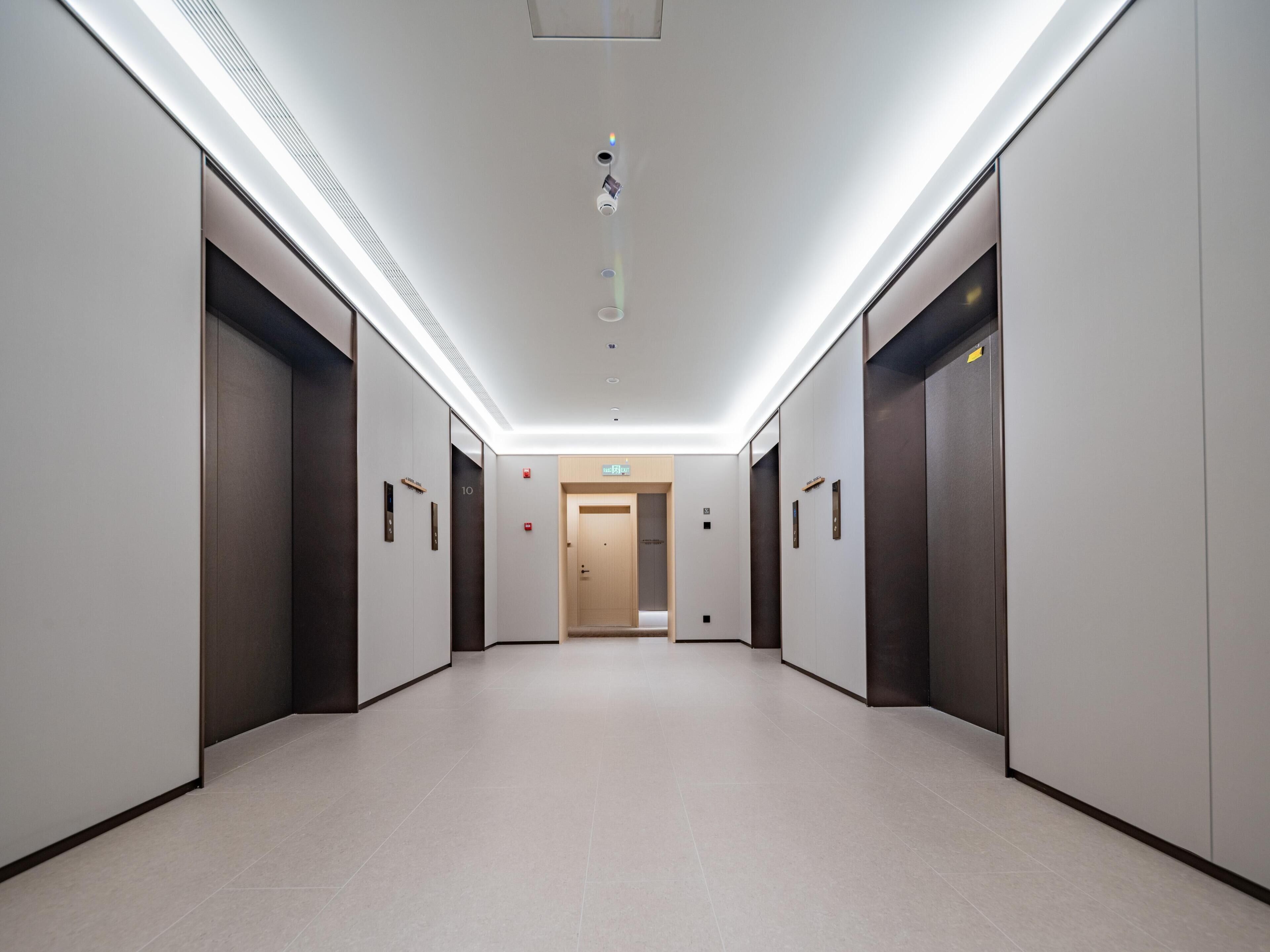 A modern hallway with elevators, a fire alarm, and a door at the end.