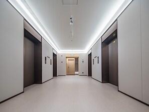 Un pasillo moderno con ascensores, un detector de incendios y una puerta al final.