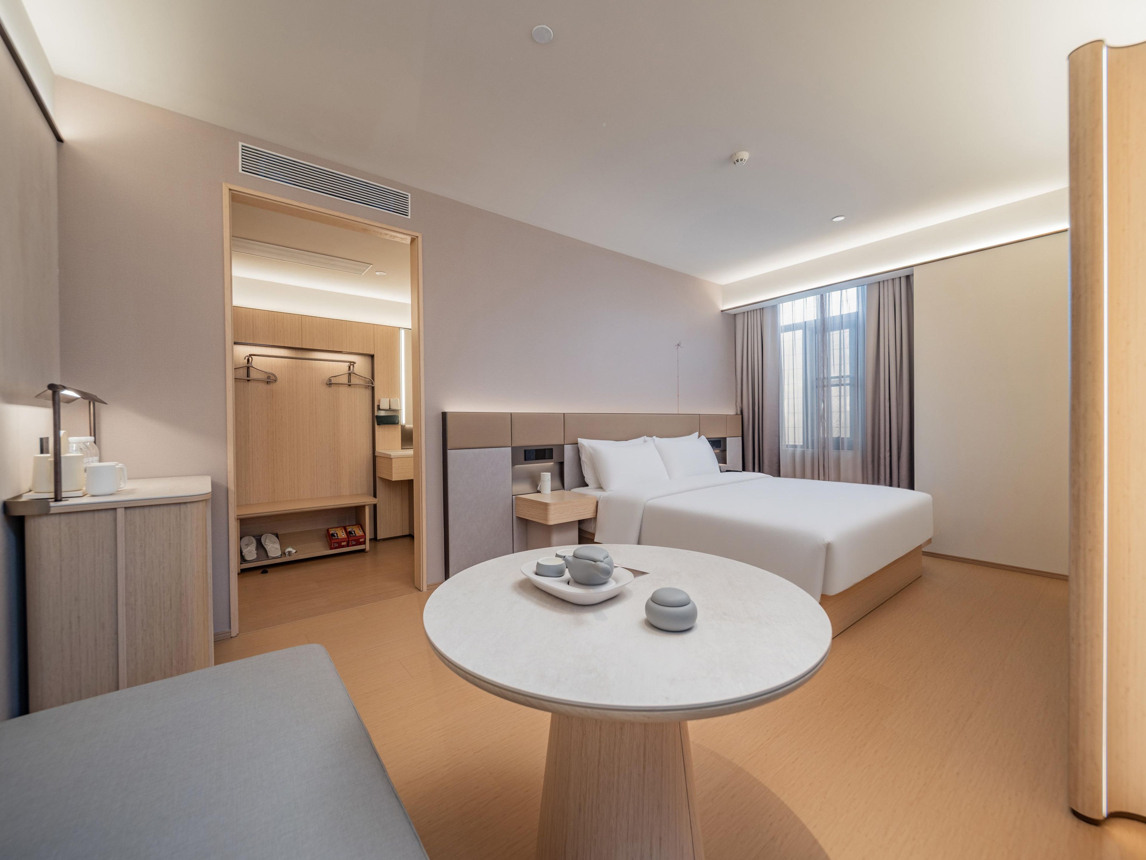 A modern hotel room with a bed, bedside table, and a round table with cups and a teapot.