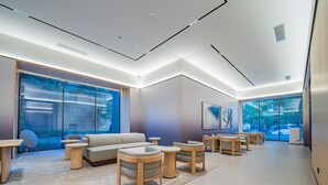 Eine moderne Hotelhalle mit einer Couch, runden Tischen und einem großen Fenster mit Blick ins Freie.