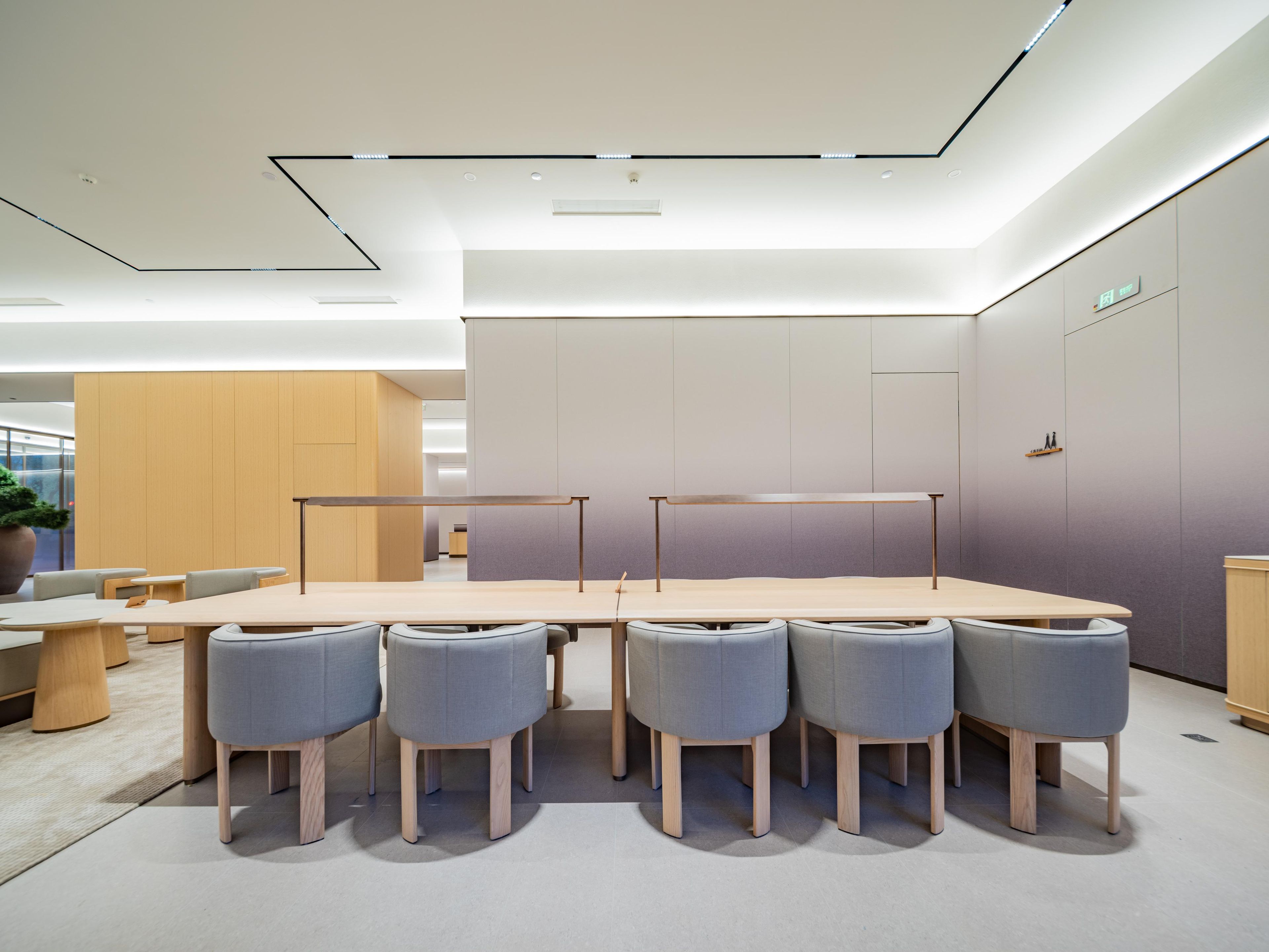 A modern conference room with a long table and six grey chairs, a wooden cabinet, and a large potted plant.