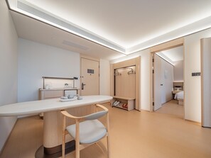 Quarto de hotel moderno com uma secretária grande, uma cadeira, um guarda-roupa e zona de duche.