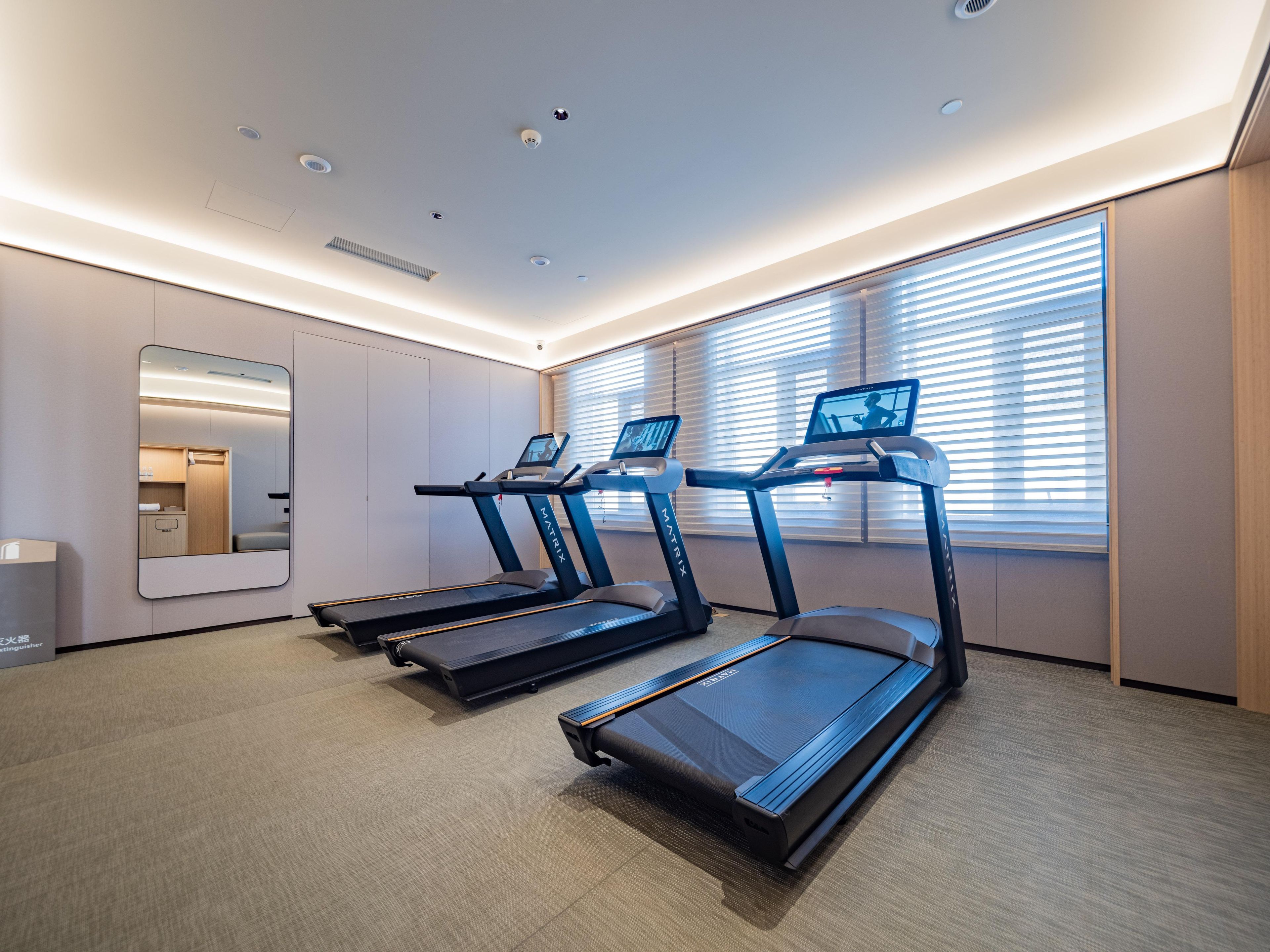 A modern fitness room with treadmills, a large mirror, and a view of the outside through large windows.
