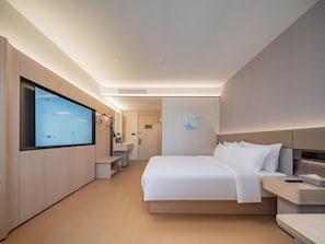 A modern hotel room with a large bed, bedside tables, a TV mounted on the wall, and a walk-in closet.