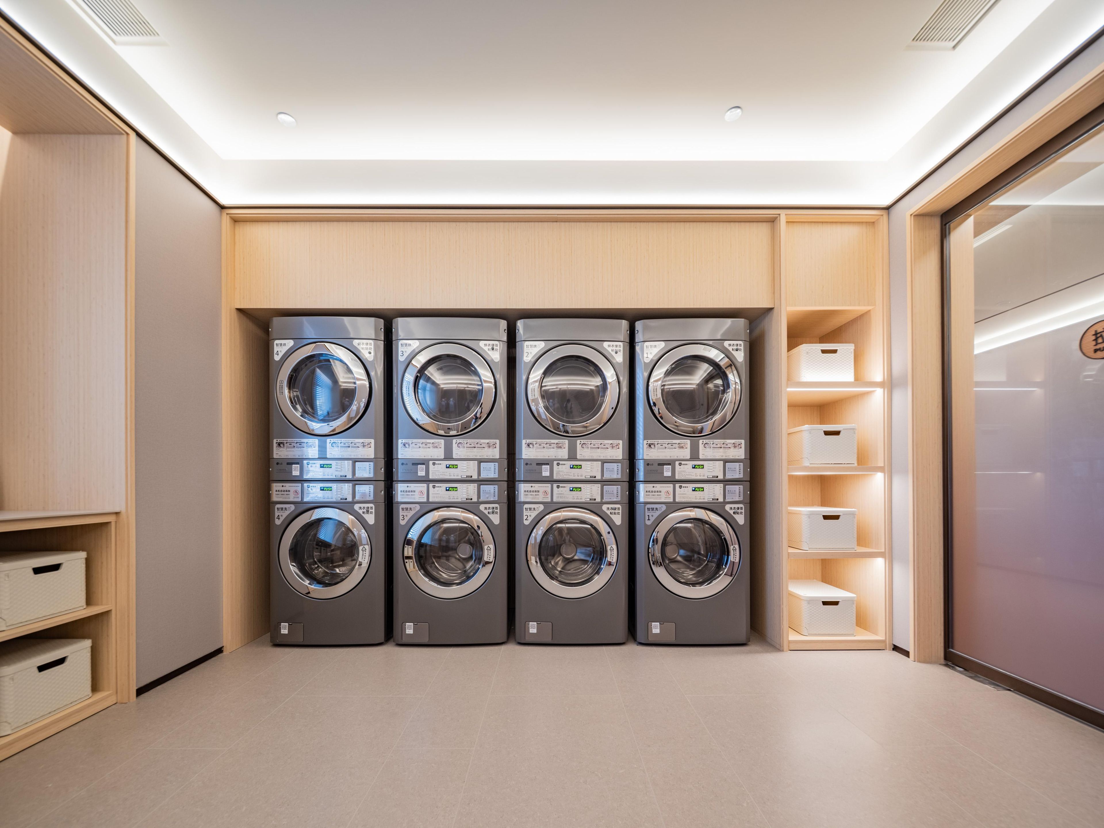 Un lavadero con cuatro lavadoras empotradas en la pared, estantes de madera y cajas de almacenamiento.
