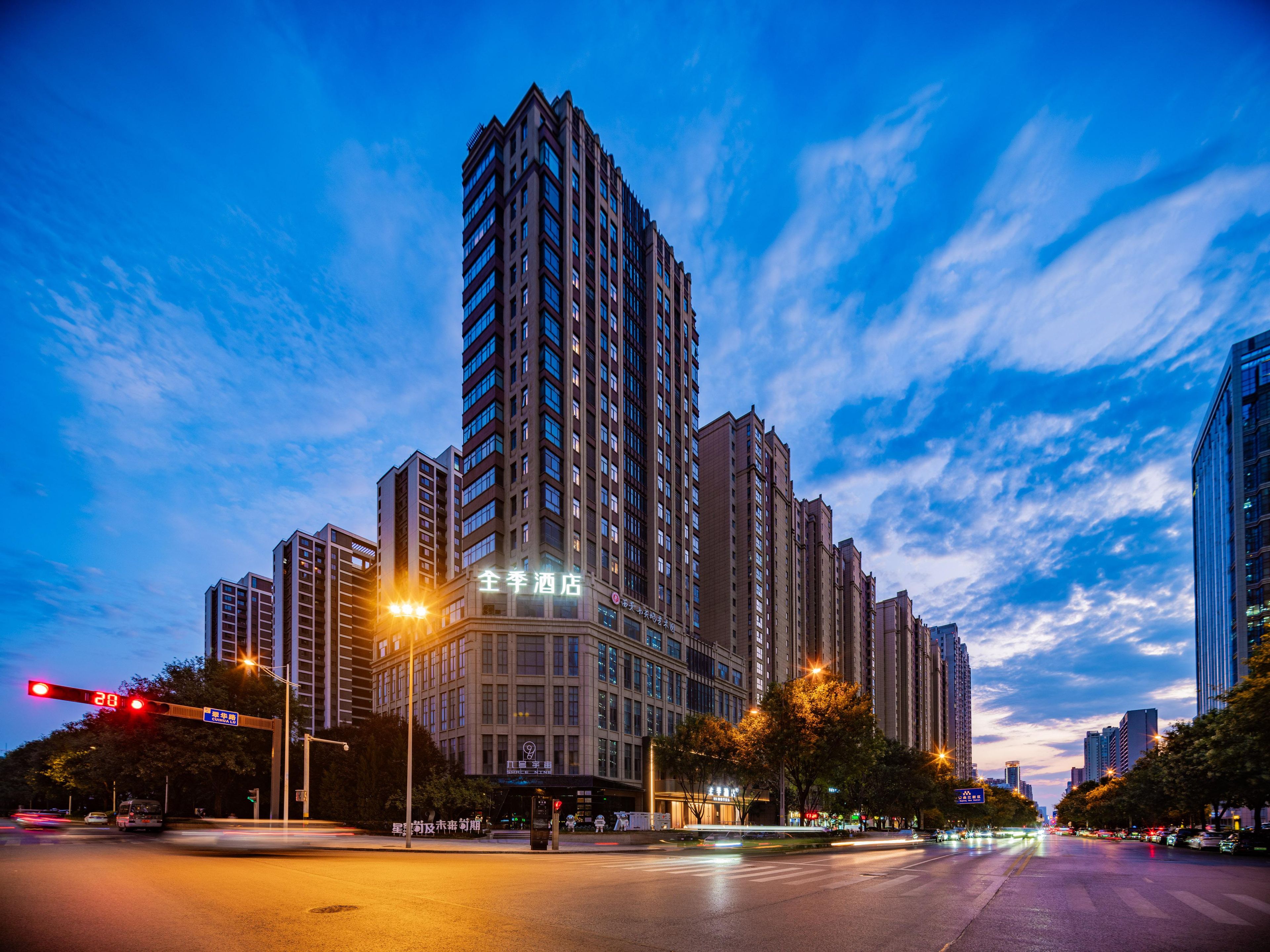 A high-rise building with multiple floors, a prominent entrance, and a clear sky with clouds.