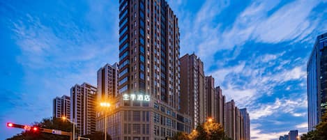 A high-rise building with multiple floors, a prominent entrance, and a clear sky with clouds.