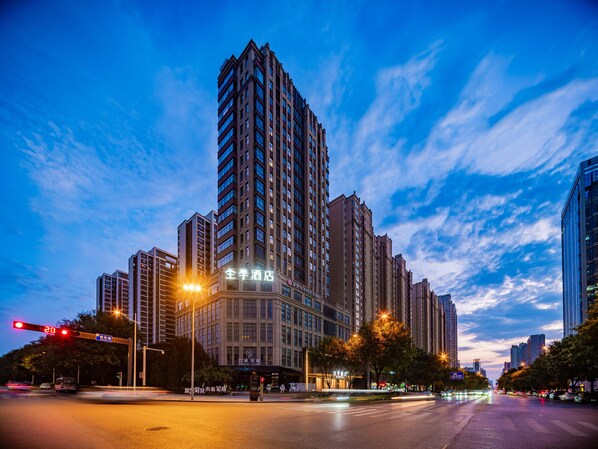 A high-rise building with multiple floors, a prominent entrance, and a clear sky with clouds.