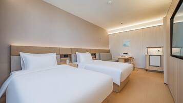 Habitación de hotel con dos camas, una mesita, una lámpara de techo y un televisor montado en la pared.