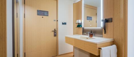 A hotel bathroom with a wooden door, a large mirror, a sink with a towel, and a toilet.