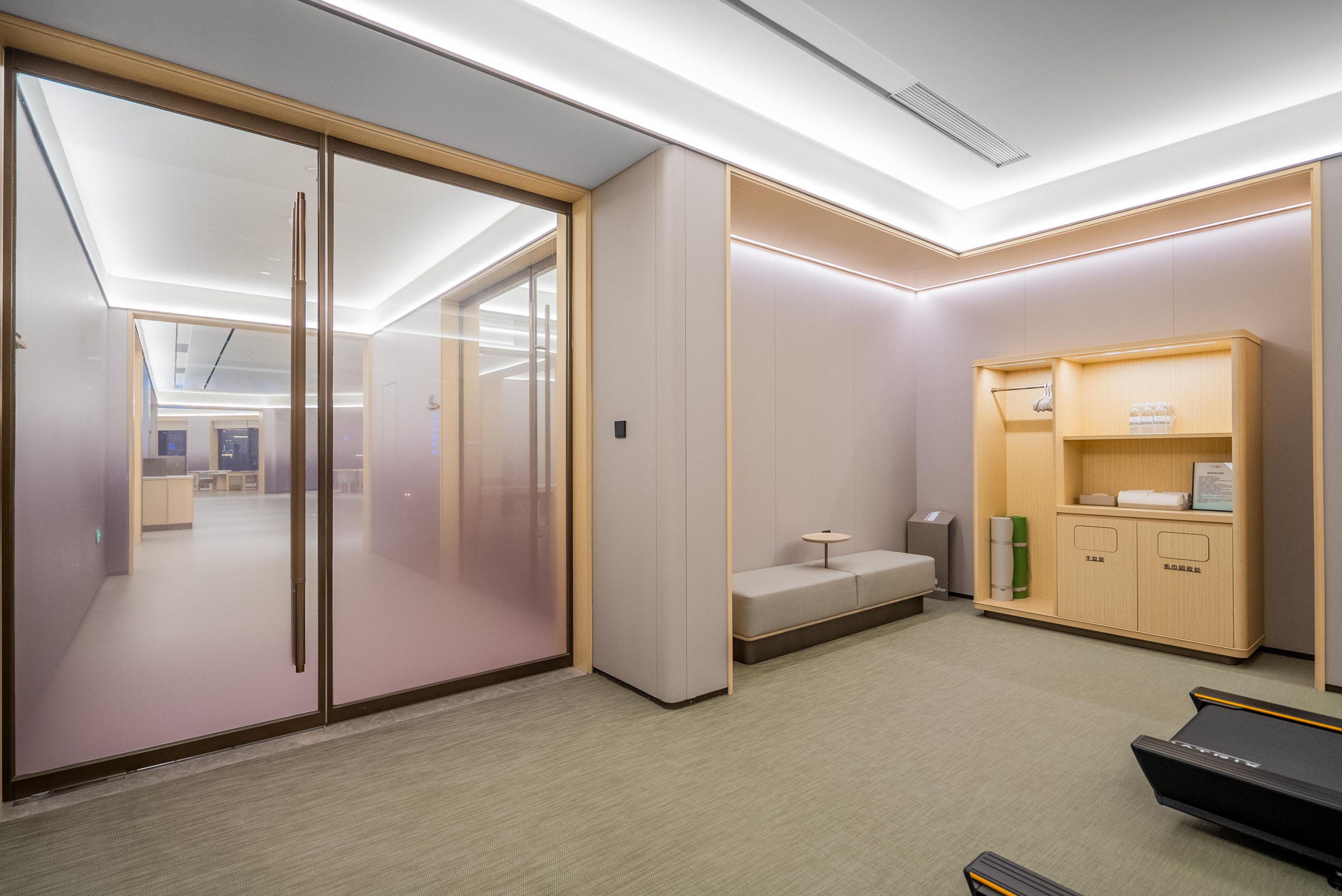 A modern office space with a glass partition, a small seating area, and a storage unit with a treadmill.