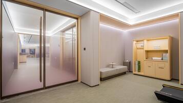 A modern office space with a glass partition, a small seating area, and a storage unit with a treadmill.