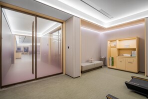 A modern office space with a glass partition, a small seating area, and a storage unit with a treadmill. - JI Hotel (xian Bell Tower Dachaishi Metro Stat (Xi'an)