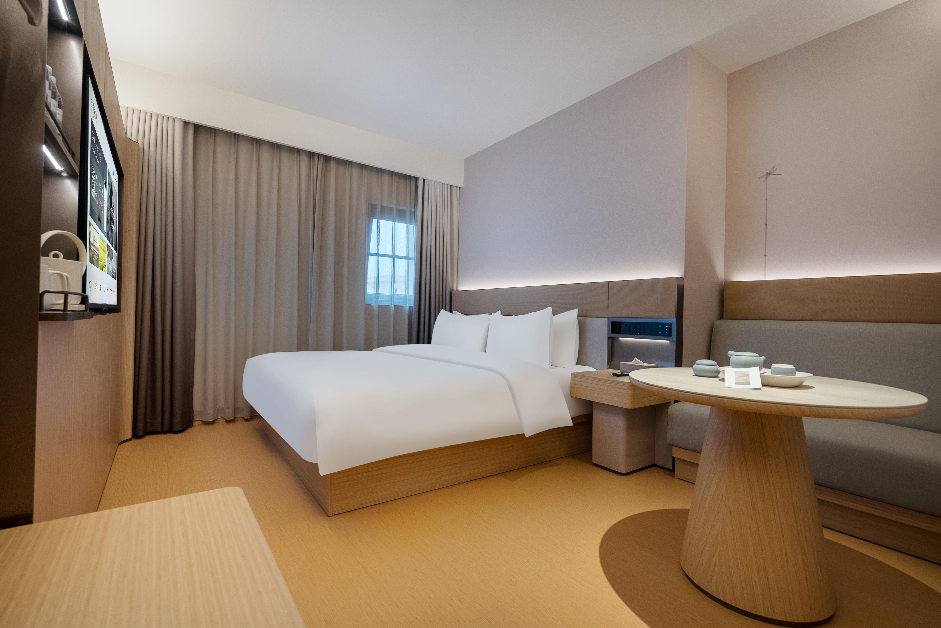 A modern hotel room with a bed, bedside table, and a round table.
