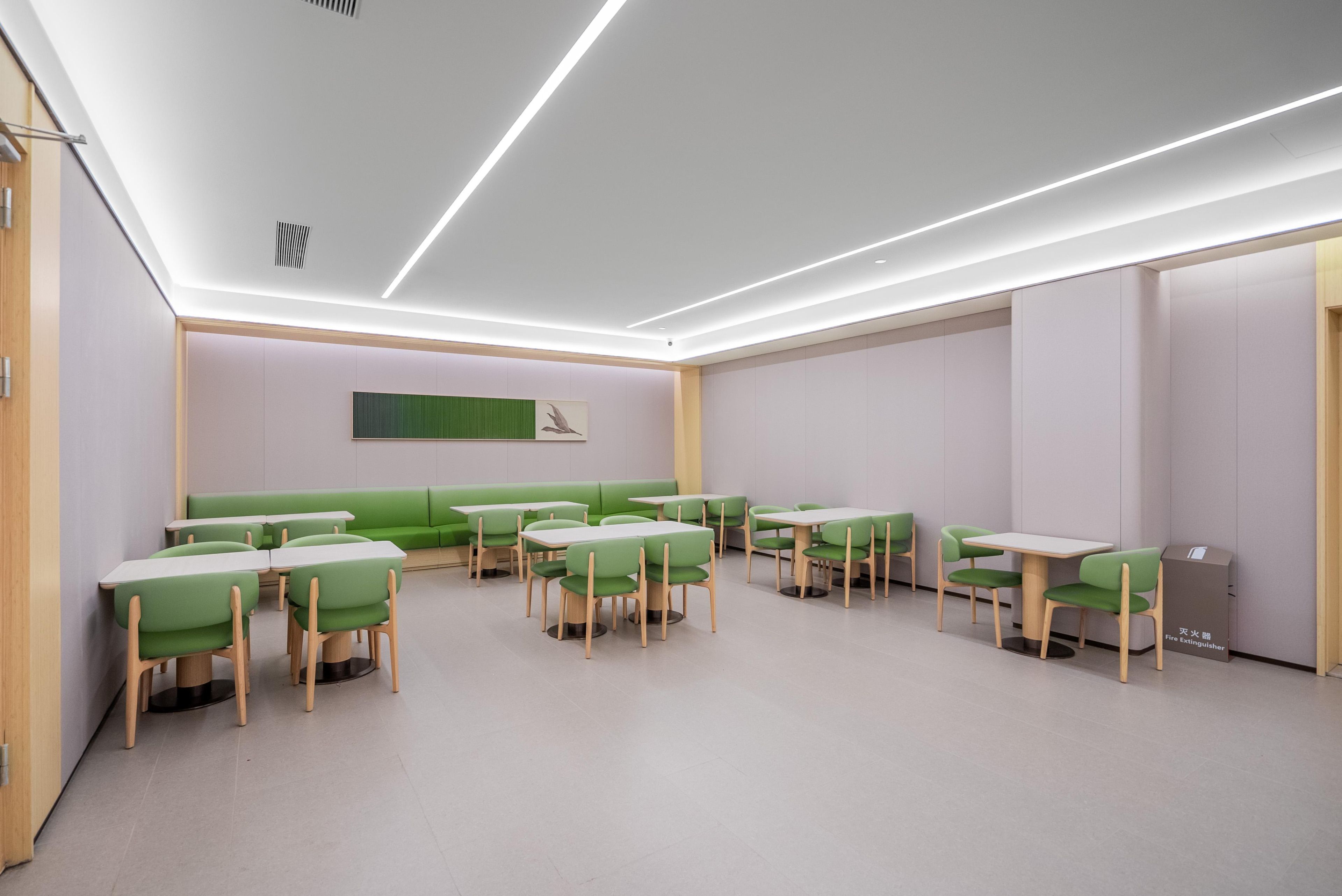 A modern interior with green seating and tables, a visible fire extinguisher, and a clean, minimalist design.