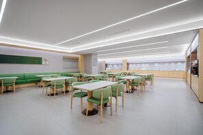 A modern dining area with green booths and tables, white ceiling lights, and a kitchen area in the background. - JI Hotel (xian Bell Tower Dachaishi Metro Stat (Xi'an)