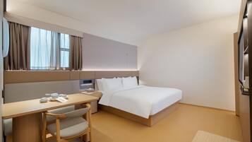 A hotel room with a bed, a desk, a chair, a bedside table, and a window with curtains.