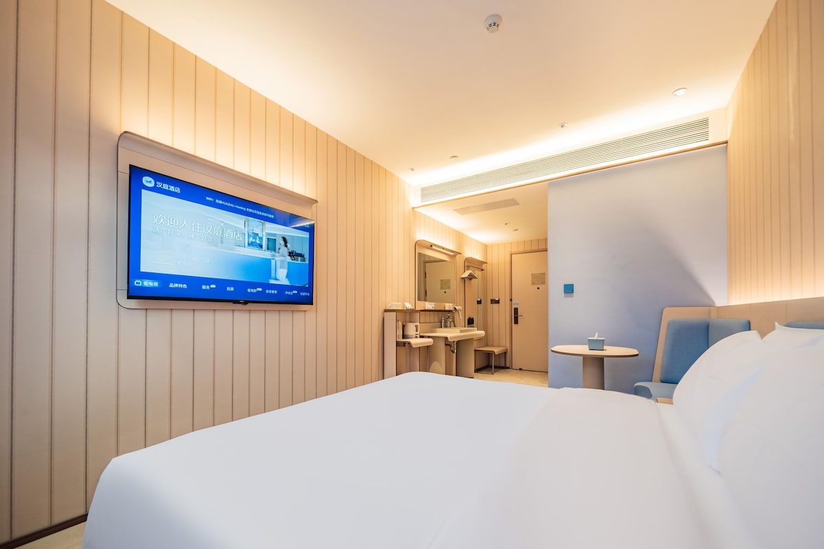 A hotel room with a large bed, a television mounted on the wall, a small table, and a chair.