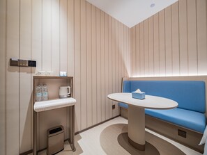 A modern hotel room with a blue sofa, a small round table, a shelf with toiletries, and a trash bin. - Hanting Hotel Xian Bell Tower Dachaishi Metro St (Xi'an)