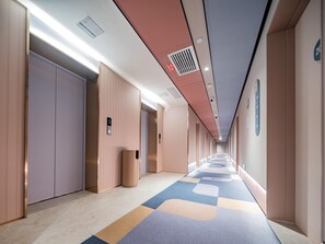 Ein Flur mit Teppichmuster, einem Mülleimer und einem an der Wand montierten Bedienfeld für den Aufzug.
