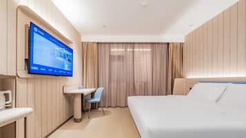 A hotel room with a bed, a desk, a chair, a television mounted on the wall, and a window with curtains.