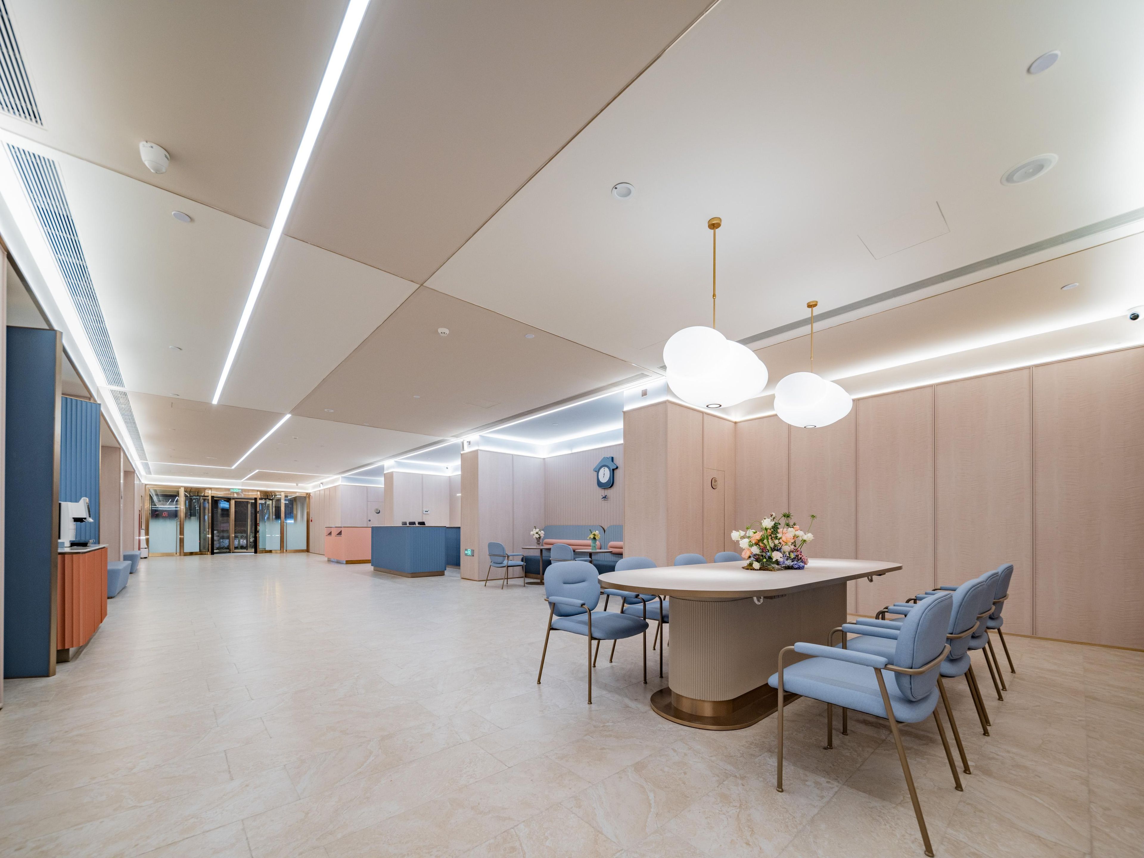 A modern hotel lobby with a reception desk, seating area, and a large table with chairs.