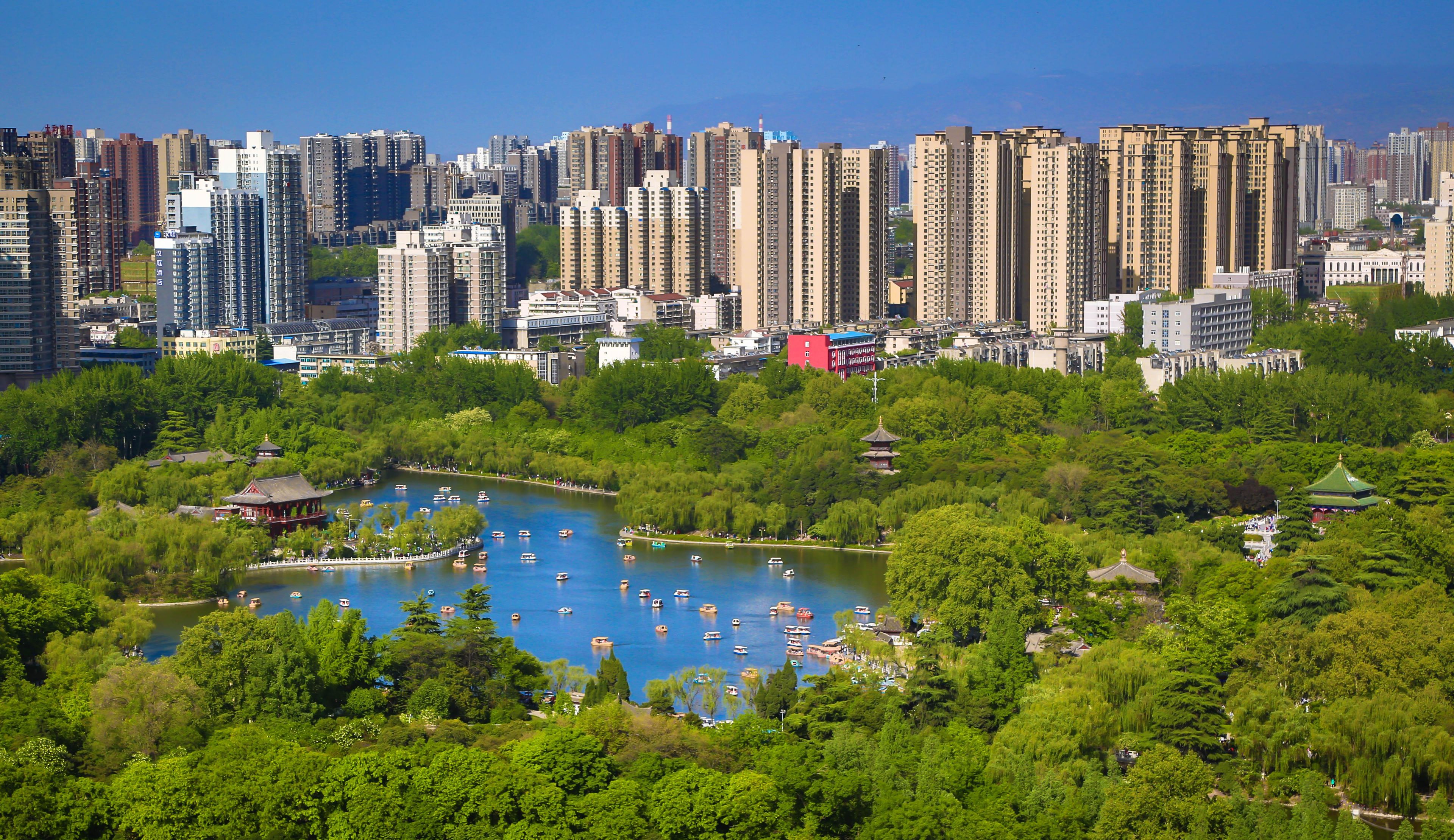A cityscape with high-rise buildings and a park with a lake and boats.