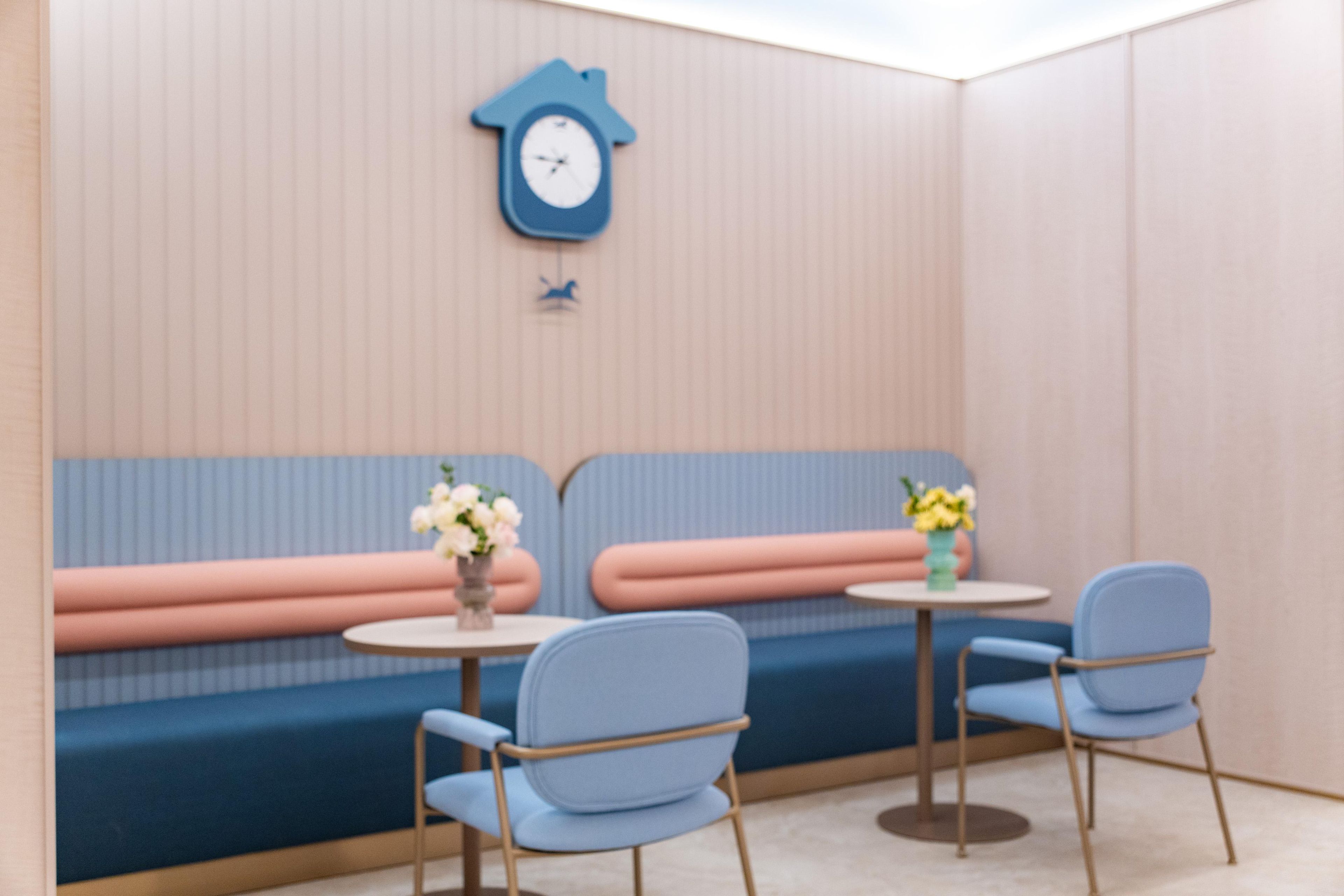 A room with a blue sofa, two chairs, a small table, and a wall clock.