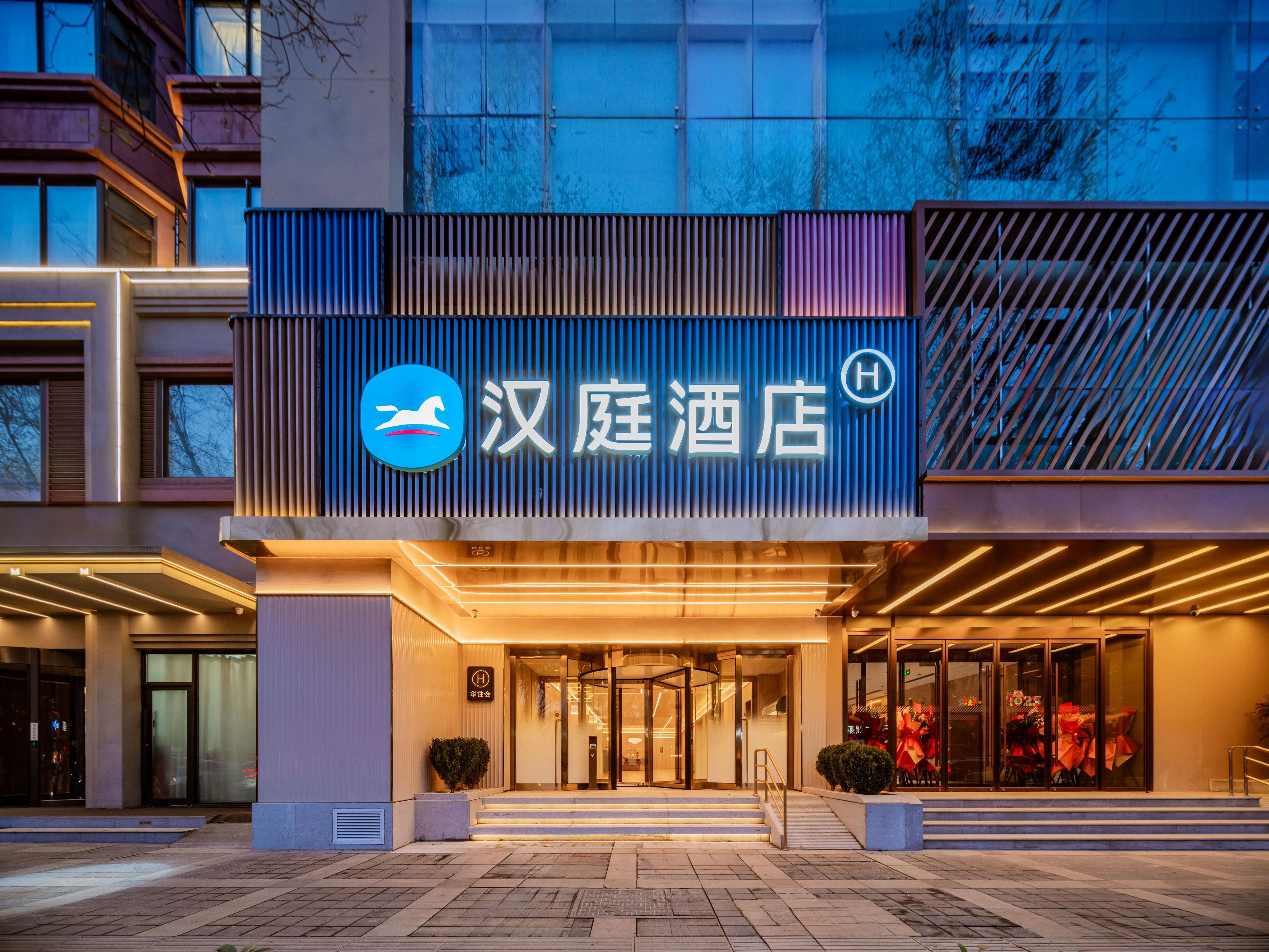 A hotel entrance with a modern facade, illuminated signage, and a glass door entrance.