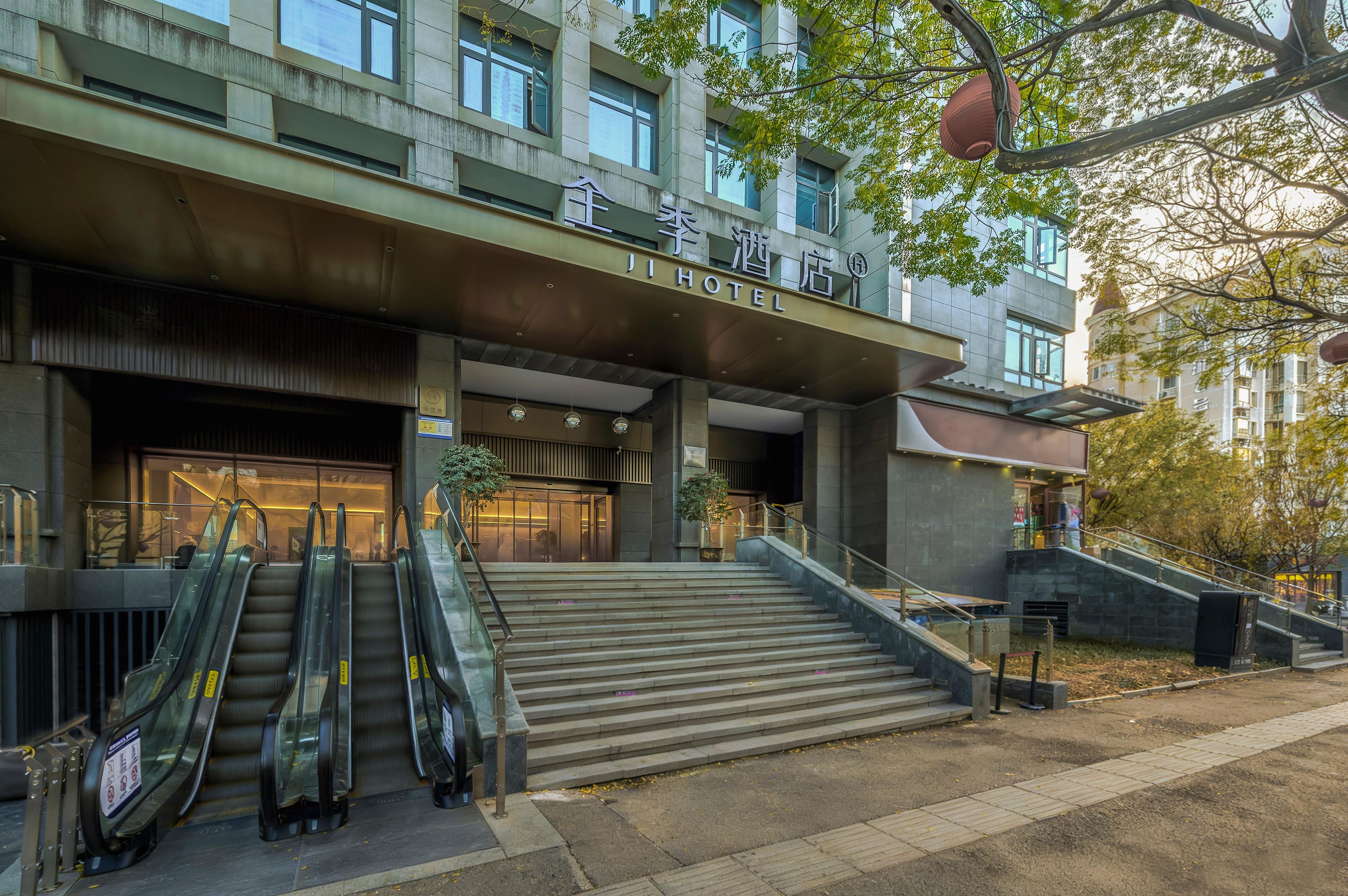 Entrada de hotel con diseño moderno, que incluye una escalera de acceso, una zona cubierta con escaleras mecánicas y un cartel con el nombre del hotel.