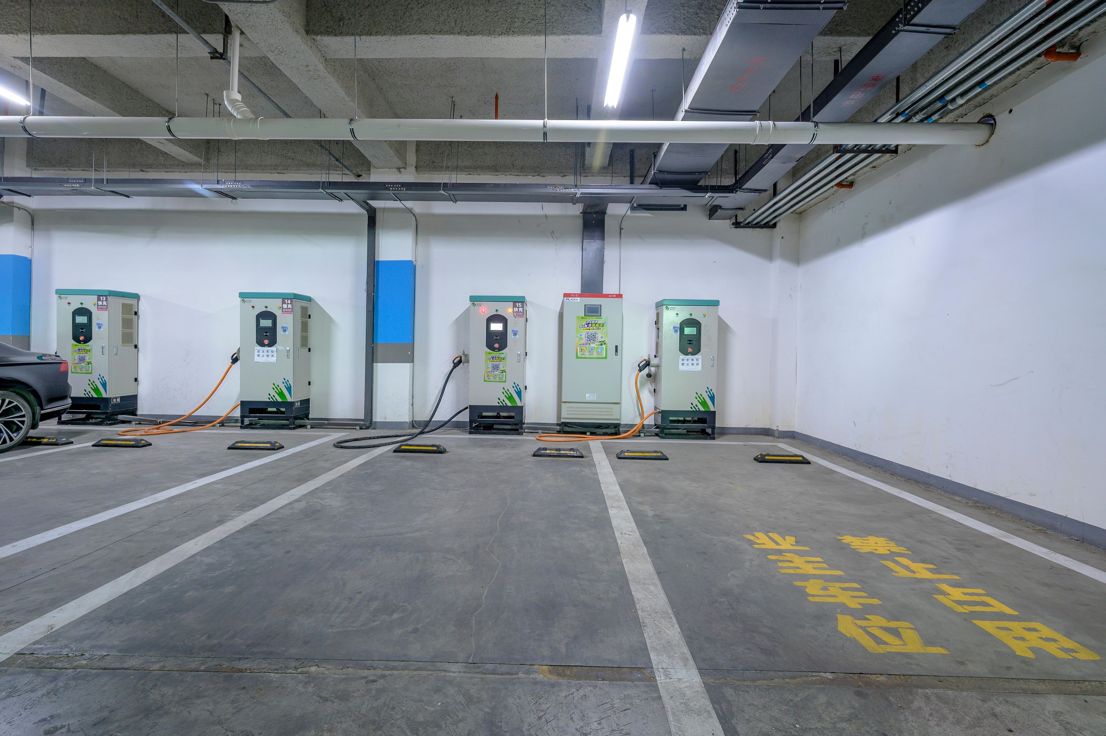 Un estacionamiento con múltiples estaciones de carga, espacios de estacionamiento delimitados y piso de concreto.