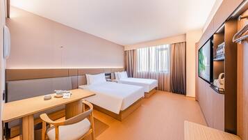 Une chambre d’hôtel avec deux lits, un bureau, une chaise, une télévision et une fenêtre avec des rideaux.