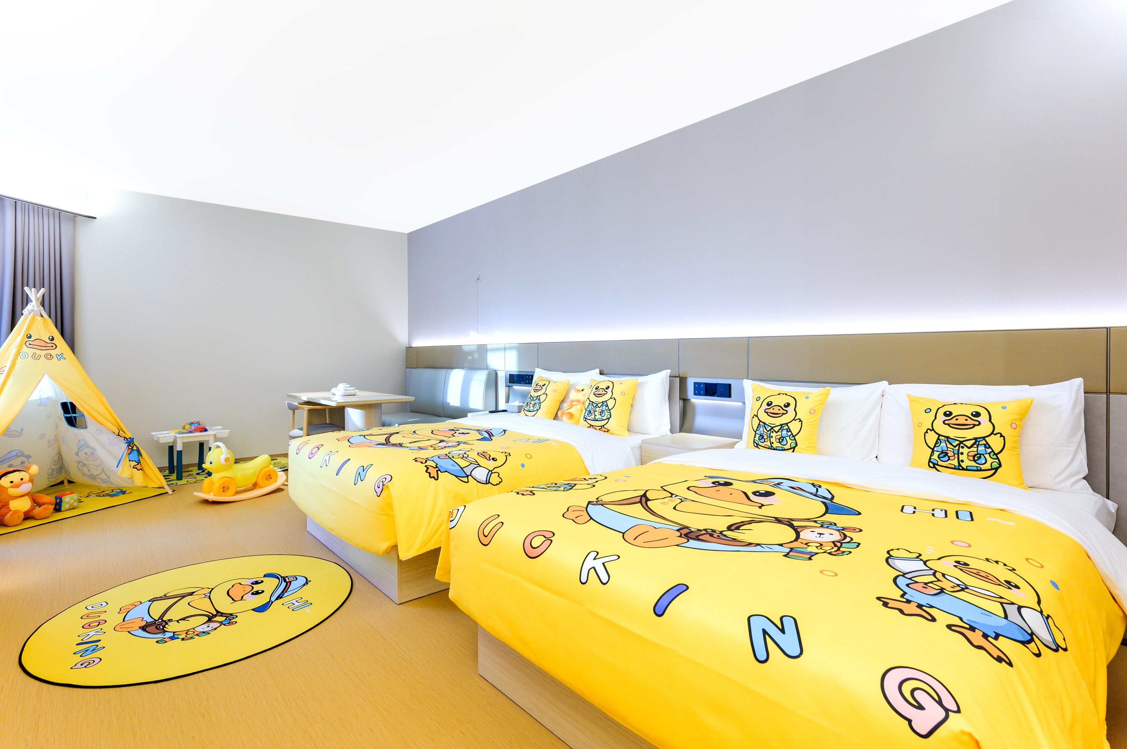 A hotel room with two beds, a desk, a chair, a small table, a yellow play tent, and a toy car.
