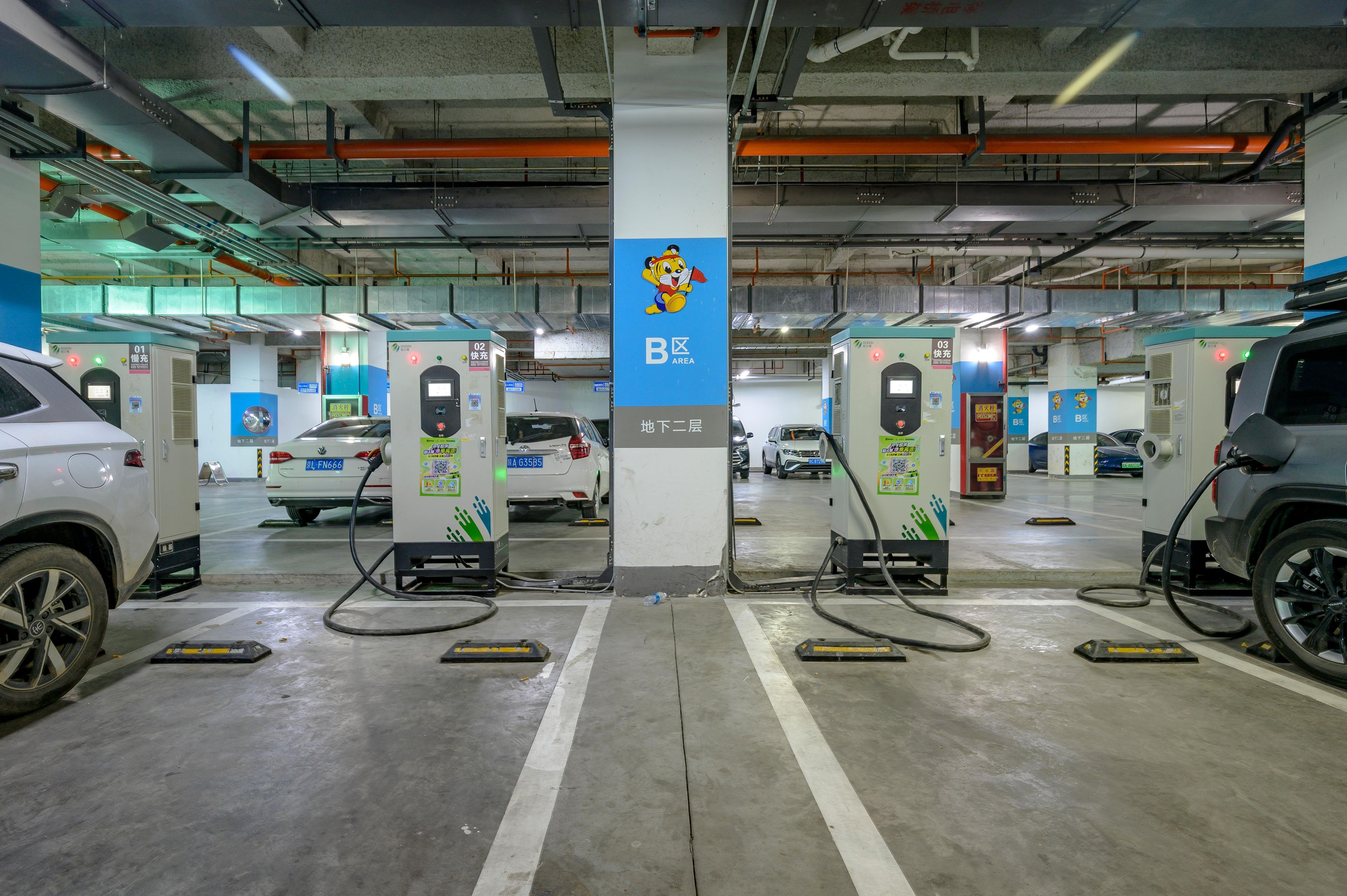 Un estacionamiento con múltiples estaciones de carga para vehículos eléctricos, identificado con la letra 'B' y un personaje de dibujos animados.