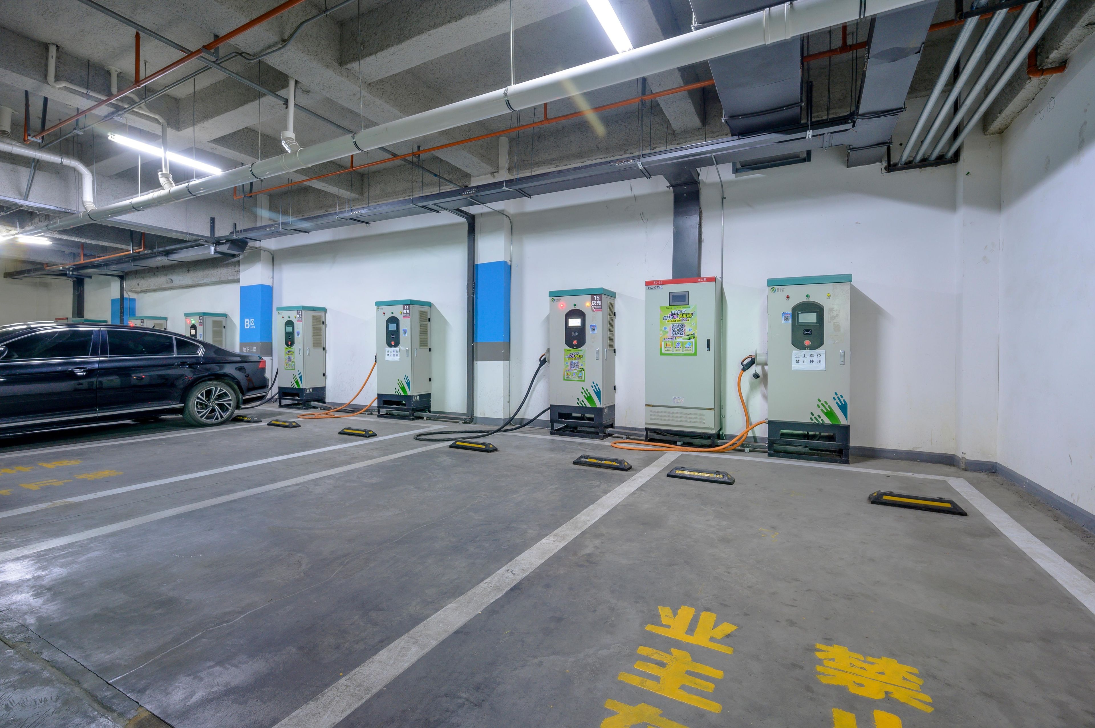 A parking garage with multiple electric vehicle charging stations, a car parked in one of the bays, and clear lane markings on the floor.