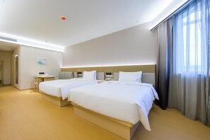 Habitación de hotel con dos camas, un escritorio, una silla y un amplio ventanal con cortinas.