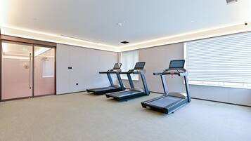 A fitness room with three treadmills, a glass door entrance, and a large window with blinds.
