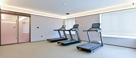 Une salle de remise en forme équipée de trois tapis de course, dotée d’une porte d’entrée en verre et d’une grande fenêtre avec des stores.