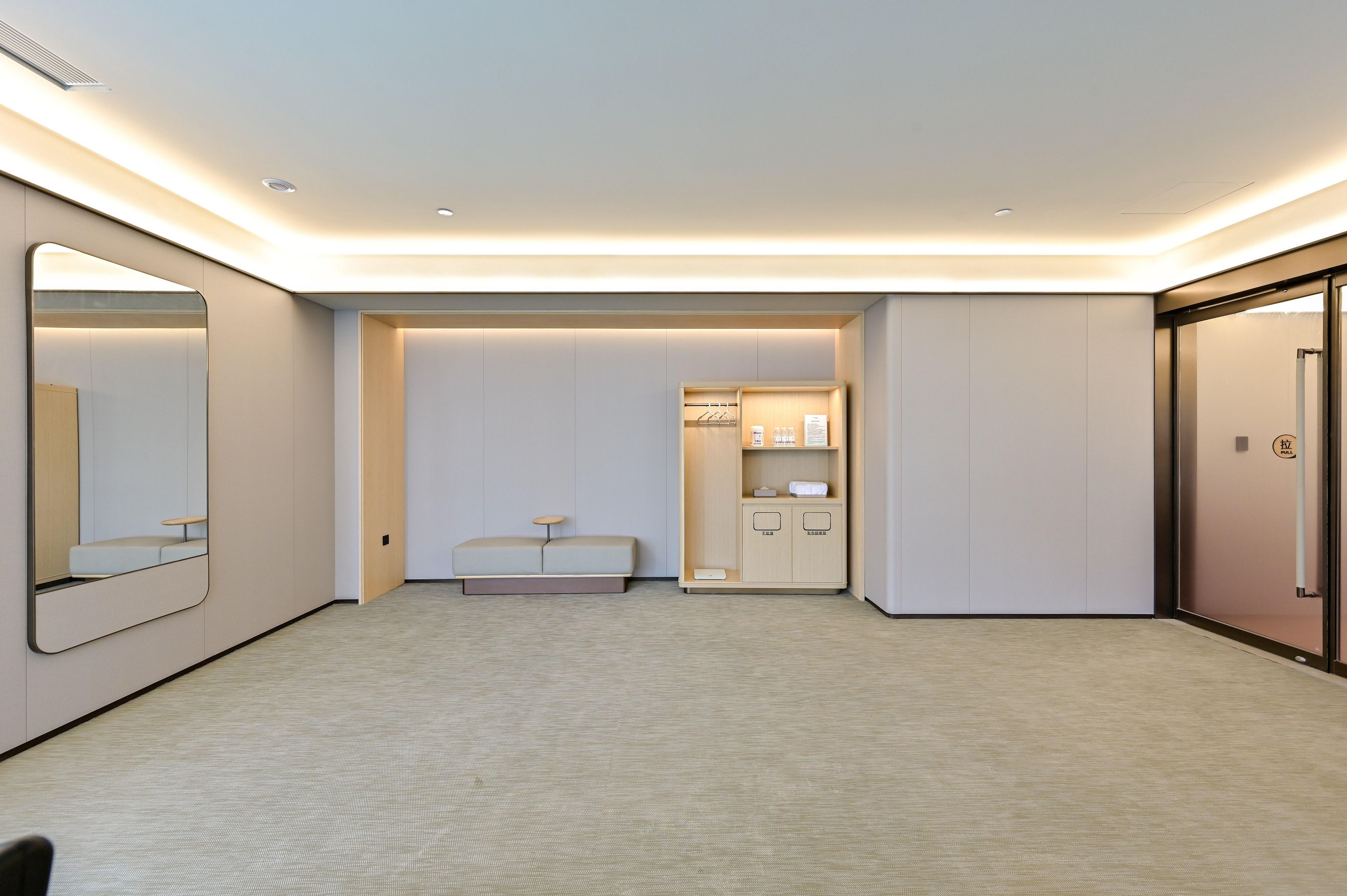 Ein Hotelzimmer mit einem großen Spiegel, einem Sofa, einem Schrank mit Pflegeprodukten und einer Tür mit Zugangsgriff.