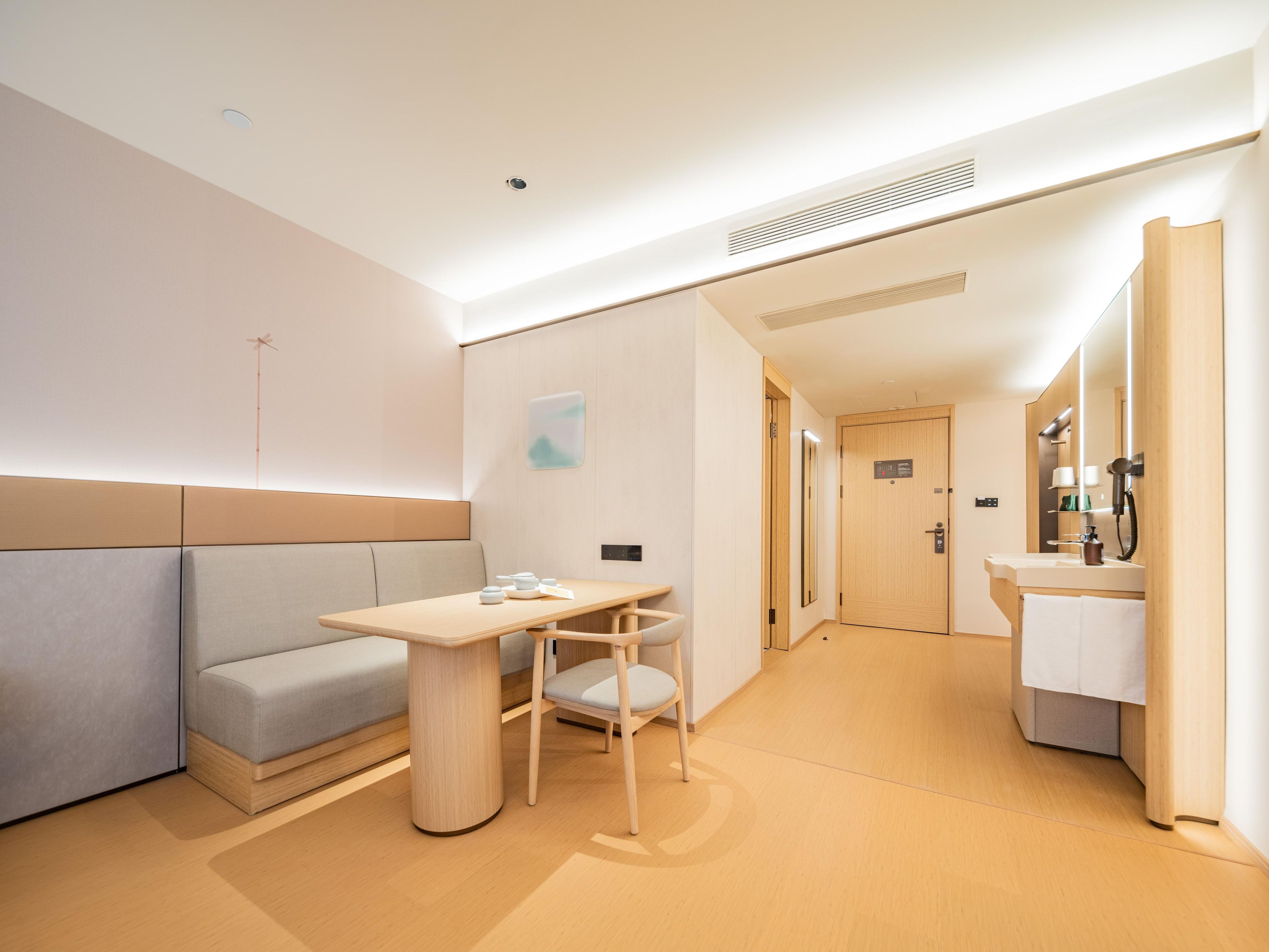 A hotel room with a sofa, a small table, a chair, a bathroom with a mirror, and a door.