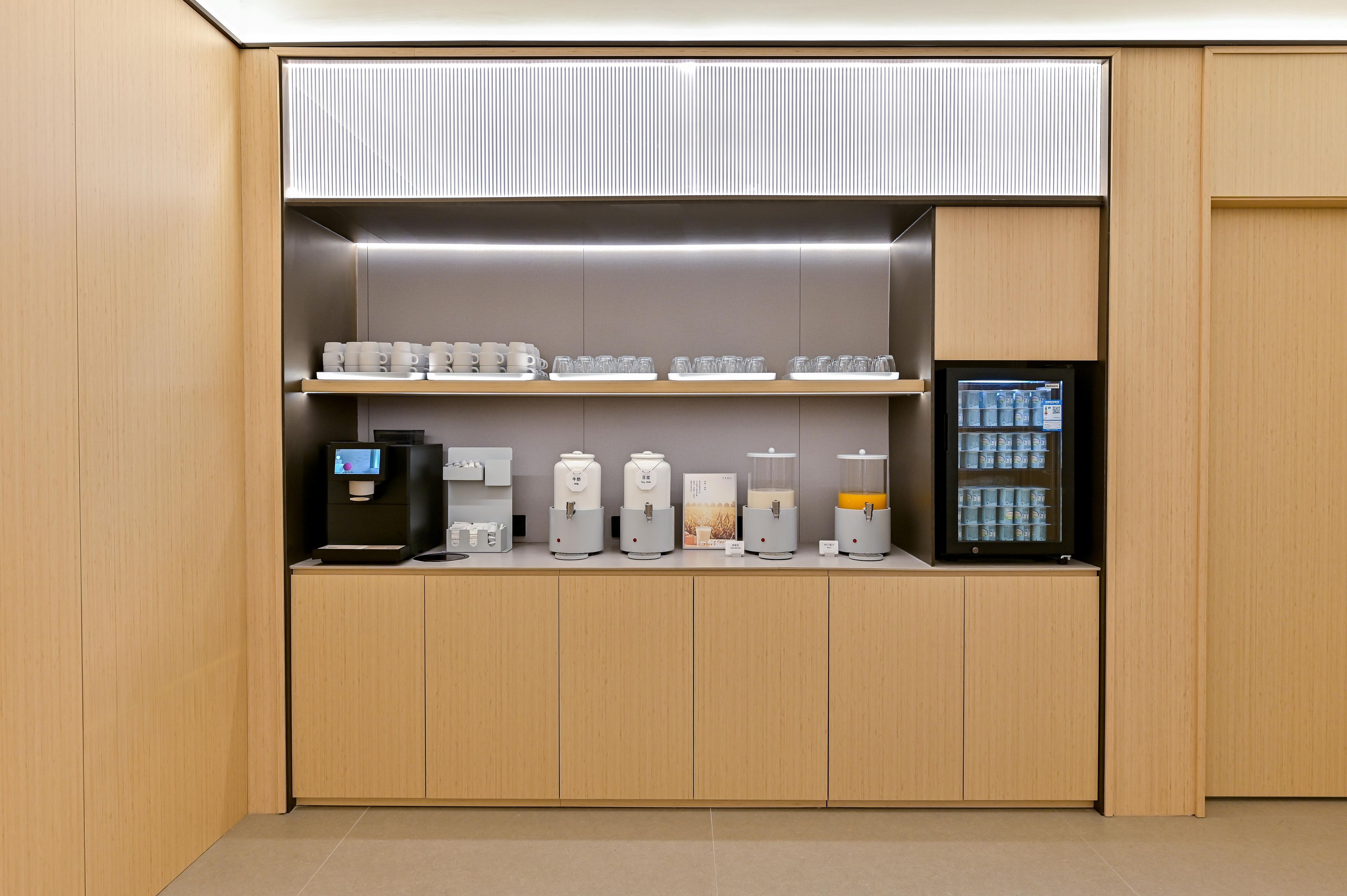 Una kitchenette moderna equipada con electrodomésticos integrados, incluyendo una cafetera, dispensadores de té y un refrigerador.