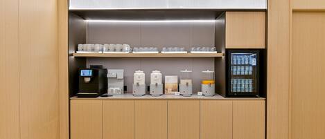 Une cuisine moderne et compacte, dotée d’appareils électroménagers intégrés, notamment une machine à café, des distributeurs de thé et un réfrigérateur.