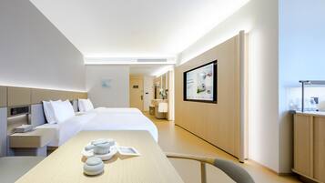 Una habitación de hotel moderna con una cama grande, mesitas de noche, un escritorio con silla, un baño con espejo y un televisor montado en la pared.