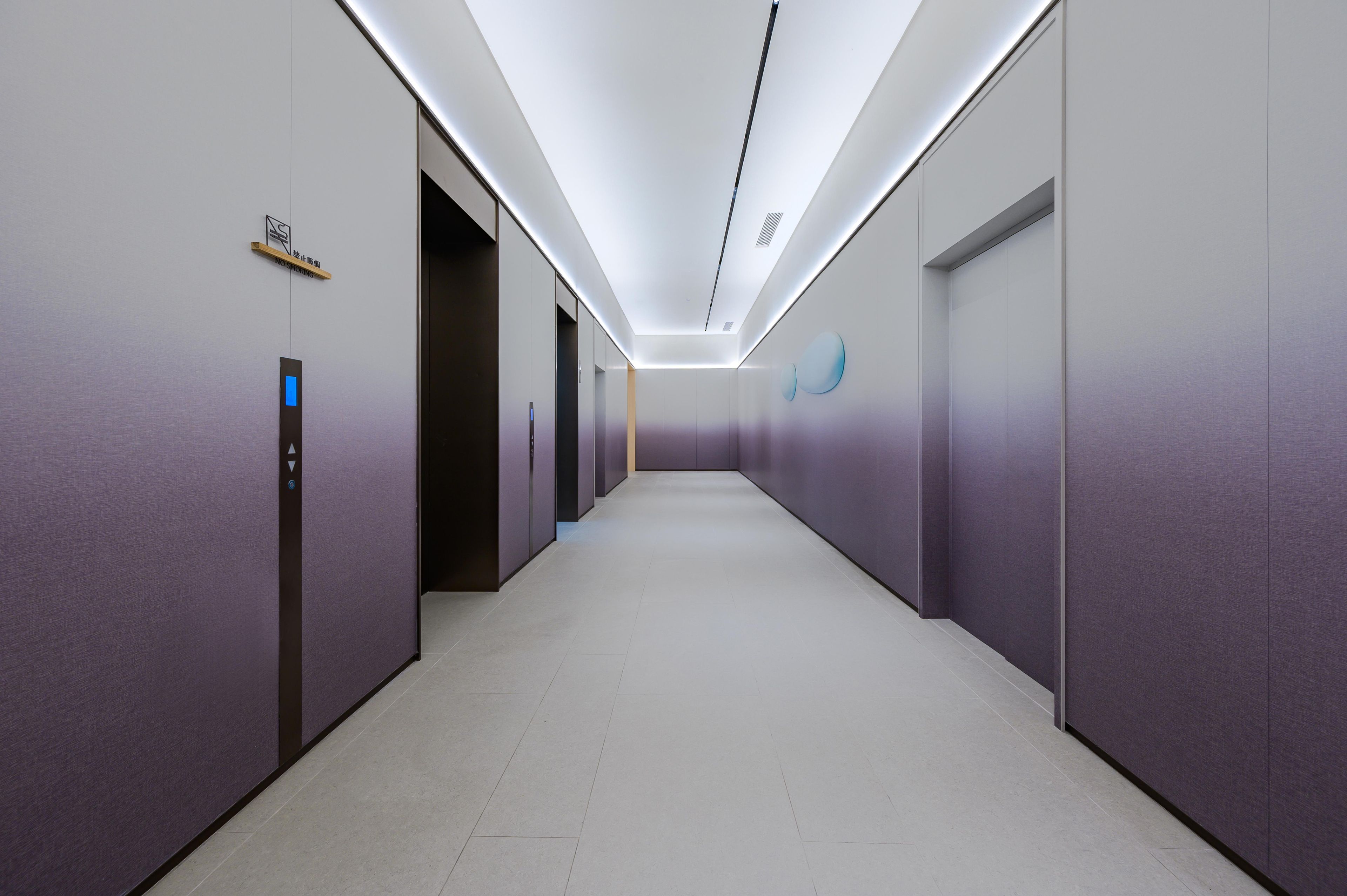 A modern hallway with a no-smoking sign, elevator, and a wall-mounted logo.