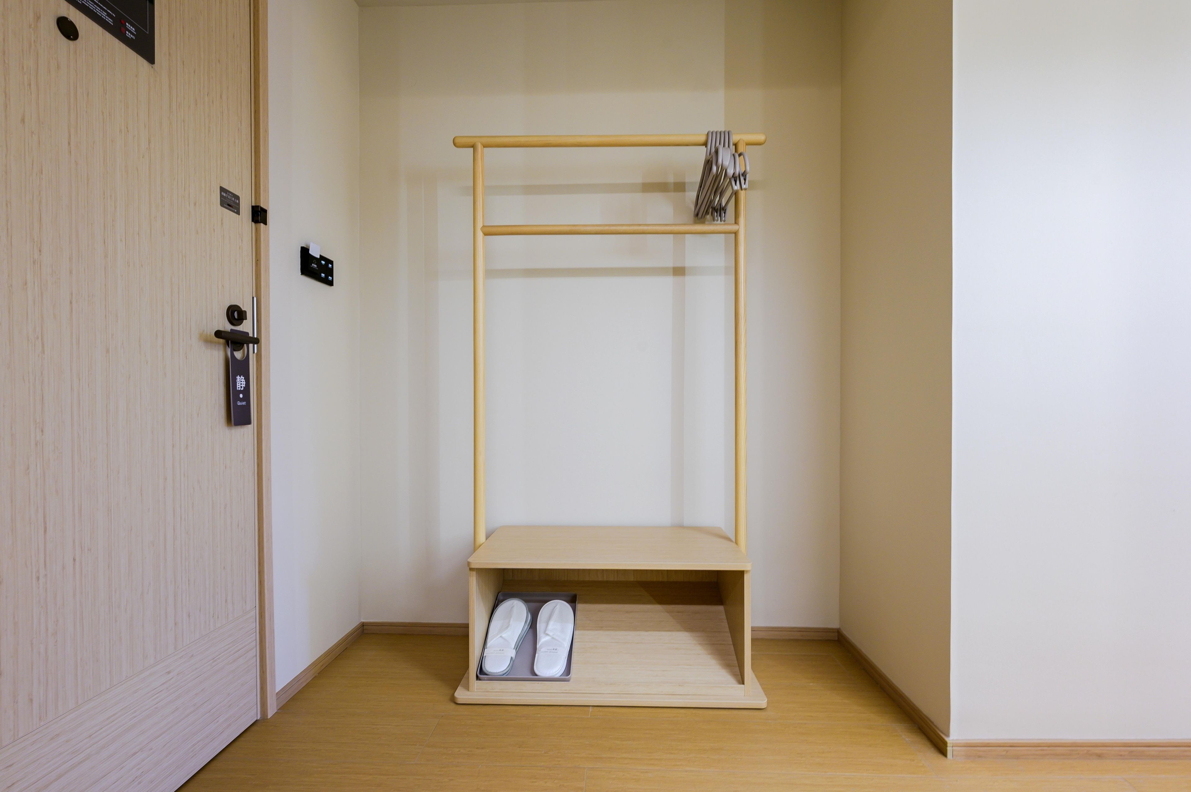 A room with a wooden door, a small shelf with slippers, and a coat rack.