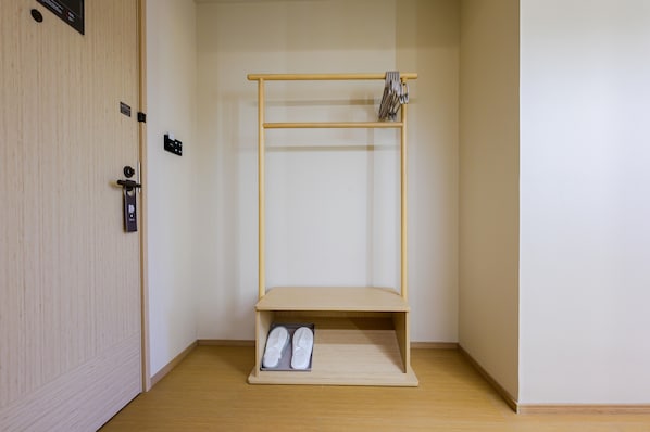 Una habitación con puerta de madera, un estante pequeño con zapatillas y un perchero.