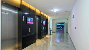 A modern elevator area with digital displays, a marble floor, and a parking entrance visible in the background.