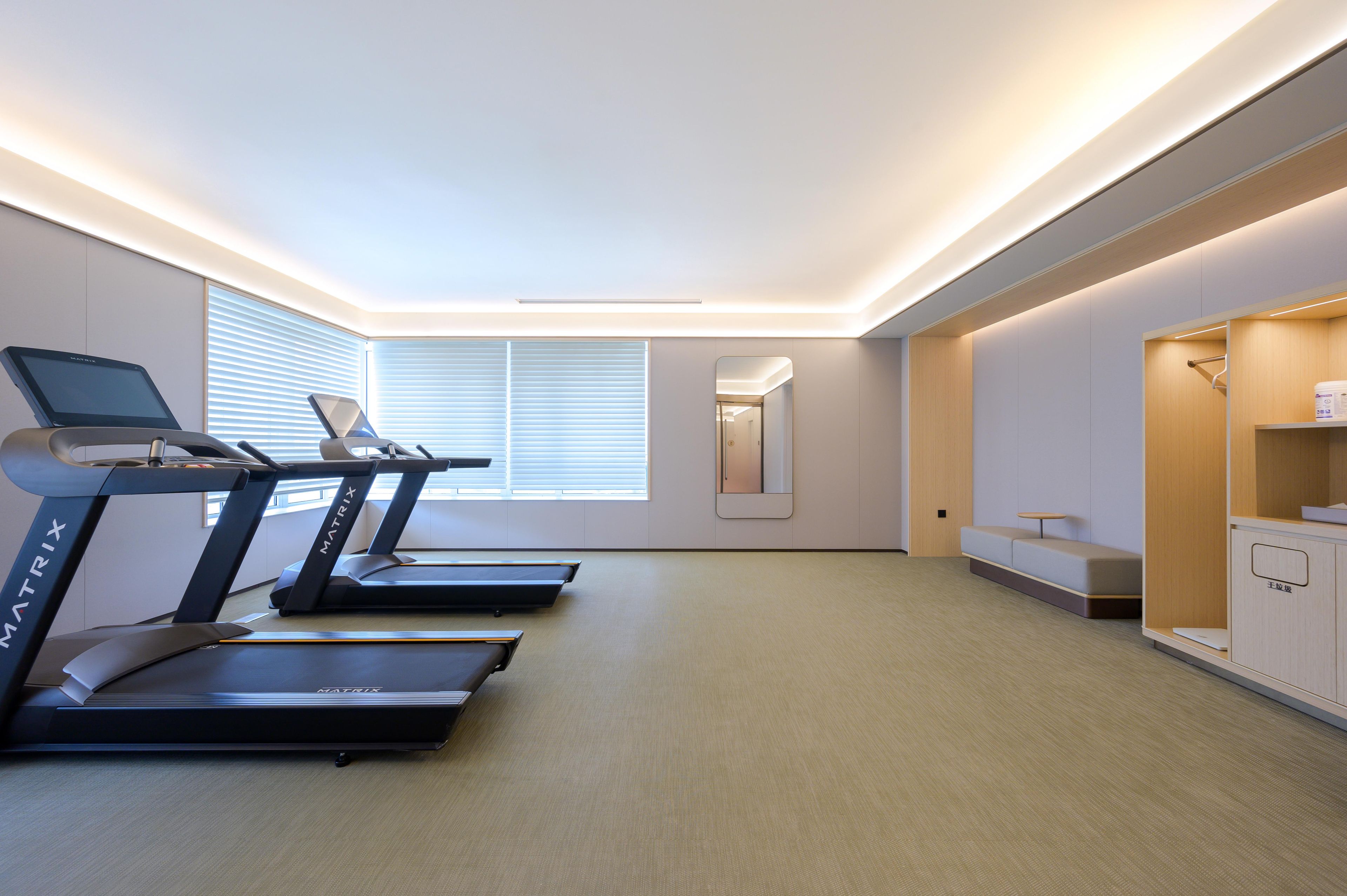 A modern fitness room with treadmills, a mirror, and a seating area.